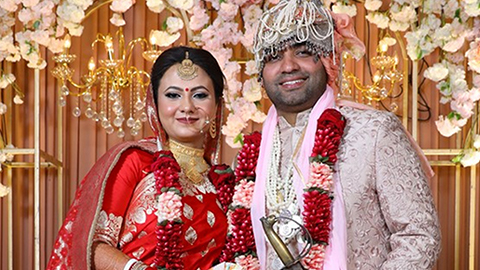 Kartik Chawla and Dibyanjana Lodh Ray pictured in wedding attire against a backdrop of flowers and chandeliers. 